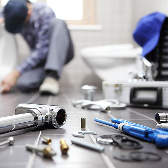 Tools and parts with a plumber in the background, working whilst insured with a sole trader insurance policy with Insure 313.